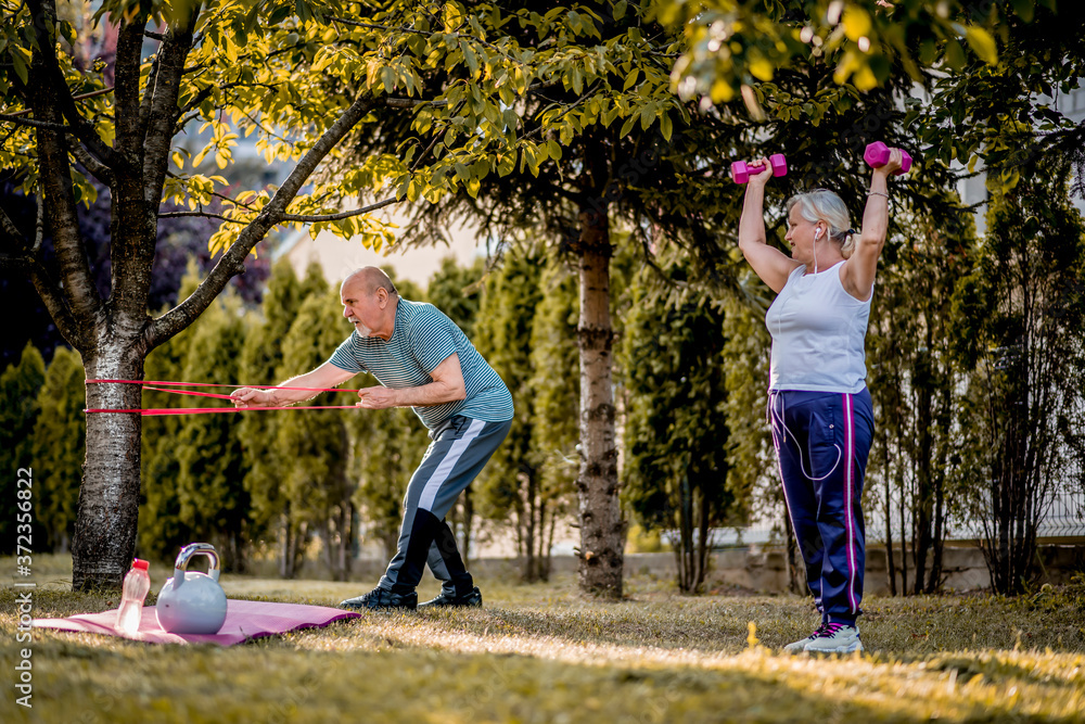 Healthy senior couple exercising with dumbbells and elastic band