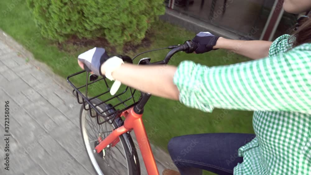 Close up first person view of a female hand rides an orange city rental bike. Woman hipster cyclist hands on handlebar riding bike, face is not visible. View from bikers eye Close up first person view of a female hand rides an orange city rental bike. Woman hipster cyclist hands on handlebar riding bike, face is not visible. View from bikers eye