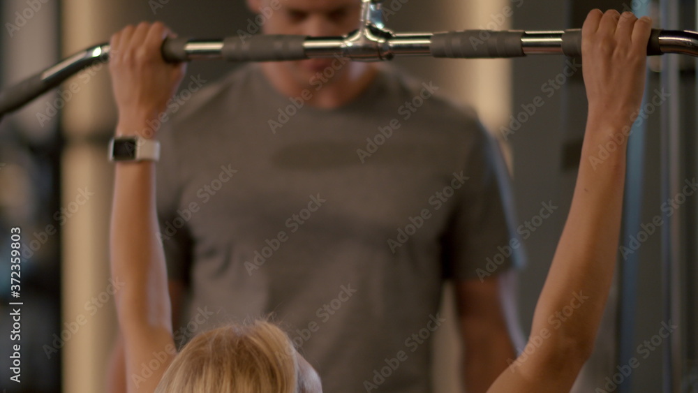 Naklejka premium Serious fit girl making pulldown in sport club. Trainer controlling client