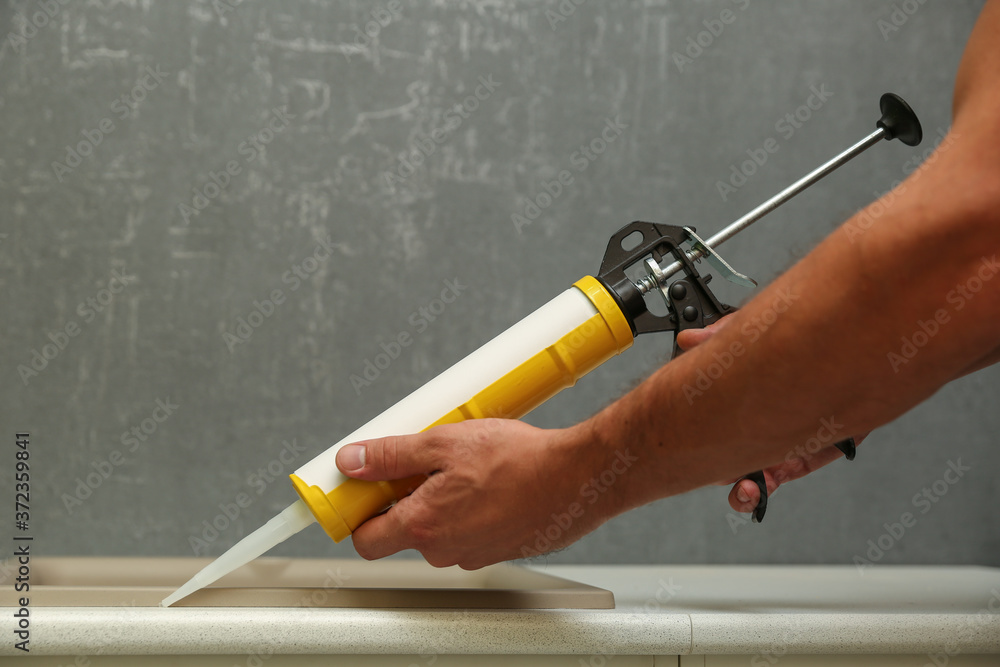 refurbishment in the apartment. kitchen sink sealing close up. worker's hands working with construction sealant gun in the kitchen refurbishment in the apartment. kitchen sink sealing close up. worker's hands working with construction sealant gun in the kitchen