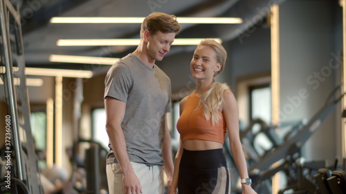 Excited couple enjoying results in sport club. Fit girl showing like sign at gym