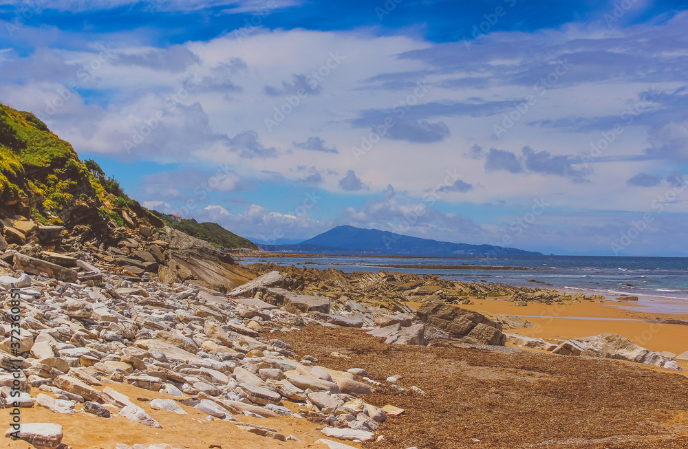 Beach sand rocks and ocean waves against blue coastal skyline