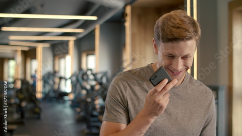 Cheerful bodybuilder speaking on phone at gym. Sportsman standing in sport club