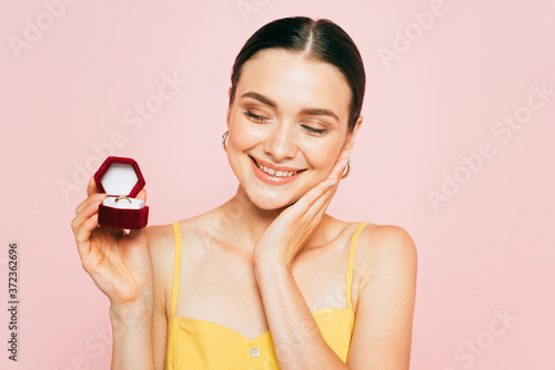brunette young woman holding box with engagement ring isolated on pink