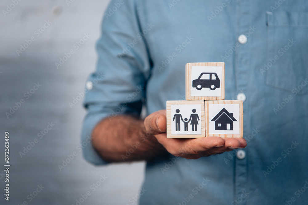 cropped view of man holding wooden cubes with car, family and house in hand cropped view of man holding wooden cubes with car, family and house in hand