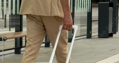 Close up of male traveler in business suit walking on railway station with white suitcase. Successful man having business trip and working meeting at another city.