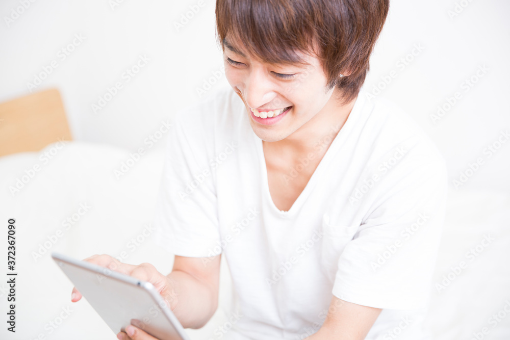 ベッドでタブレットPCを見る男性 ベッドでタブレットPCを見る男性