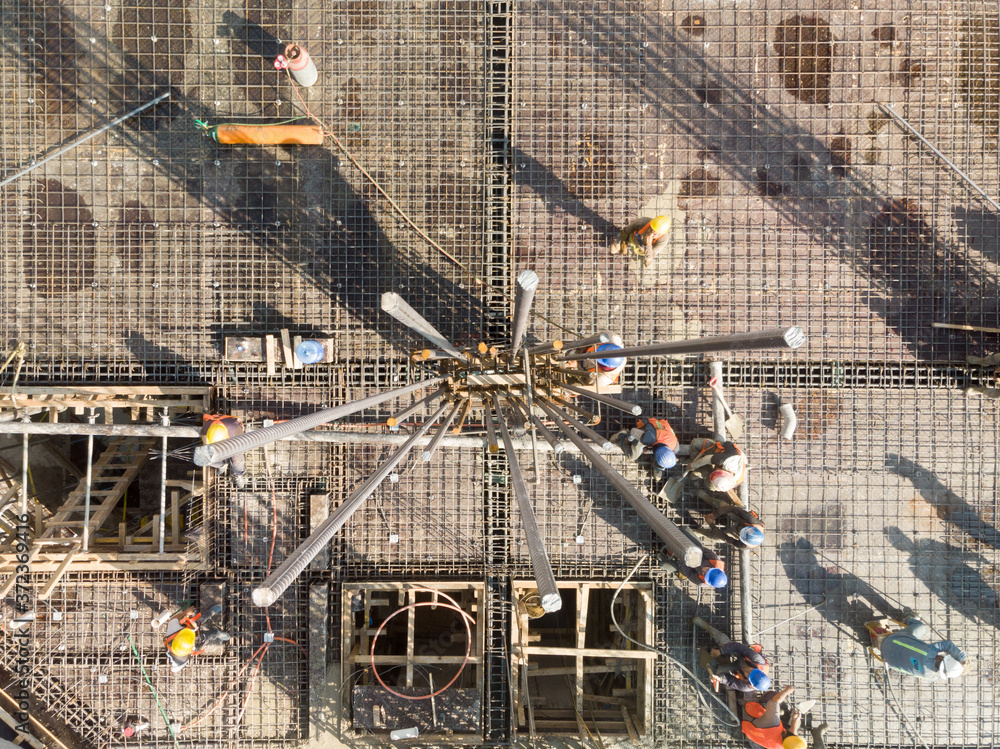 Vista aérea cential sobre el armado de una columna en una obra en construcción con obreros trabajando en segundo plano.