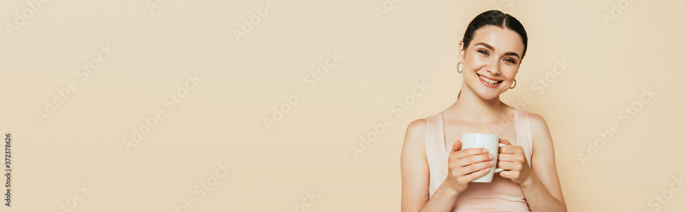 brunette young woman holding mug isolated on beige, panoramic shot brunette young woman holding mug isolated on beige, panoramic shot