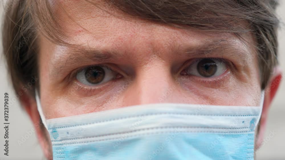 Close-up cropped portrait view of a Caucasian man wearing a face mask during Covid-19 Coronavirus pandemic. Guy in virus proof medical mask on face, looking at camera while on isolation at home. Close-up cropped portrait view of a Caucasian man wearing a face mask during Covid-19 Coronavirus pandemic. Guy in virus proof medical mask on face, looking at camera while on isolation at home.