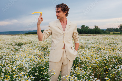 Tall handsome man standing in camomile flowers field and posing with yellow sunglasses © Smile
