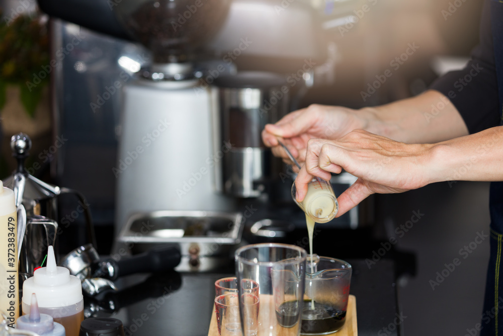 Barista's hand is pouring milk in a measuring cup.