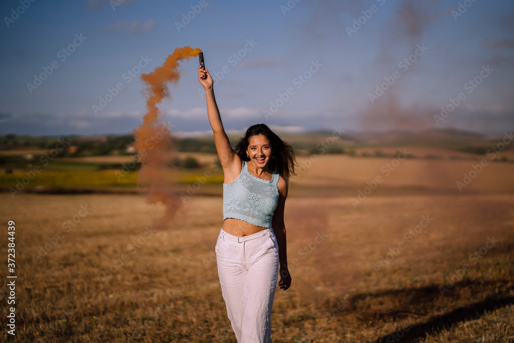 Chica joven con bengala de humo en un campo caminando