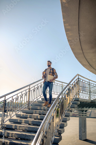 Man with laptop and coffee going downstairs