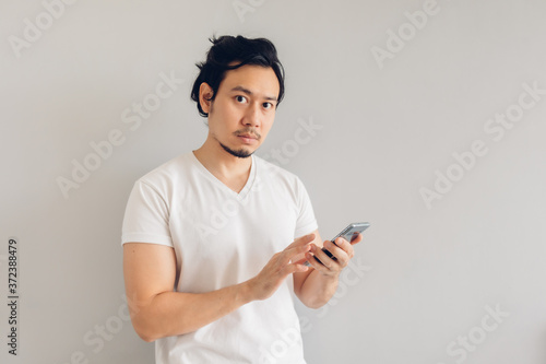 Long hair Asian man in white casual t-shirt is using smartphone. © Sevendeman