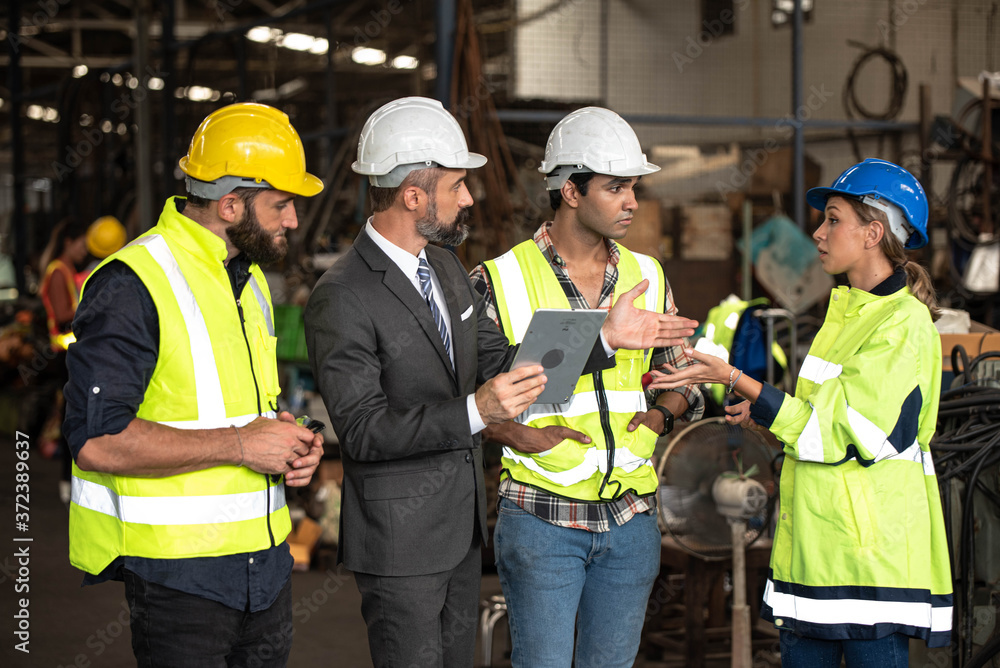 Group of factory workers consists of Manager, Engineers, Technicians with hardhat and vest jacket, discussing about industrial factory production management by using computer notebook for information Group of factory workers consists of Manager, Engineers, Technicians with hardhat and vest jacket, discussing about industrial factory production management by using computer notebook for information