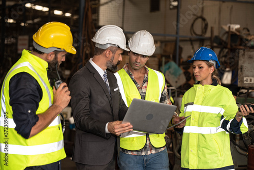 Group of factory workers consists of Manager, Engineers, Technicians with hardhat and vest jacket, discussing about industrial factory production management  by using computer notebook for information