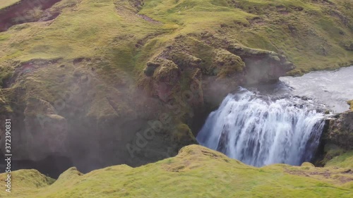 Dron panorama of a wonderful waterfall in the Skógá river canyon in Iceland. Green grass, cristalclear water and some mist comming from de water (Approaching to the waterfall and the mist) photo