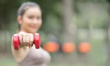 Closeup sportswoman hand holding forward red dumbbell while workout in the park, copy space.