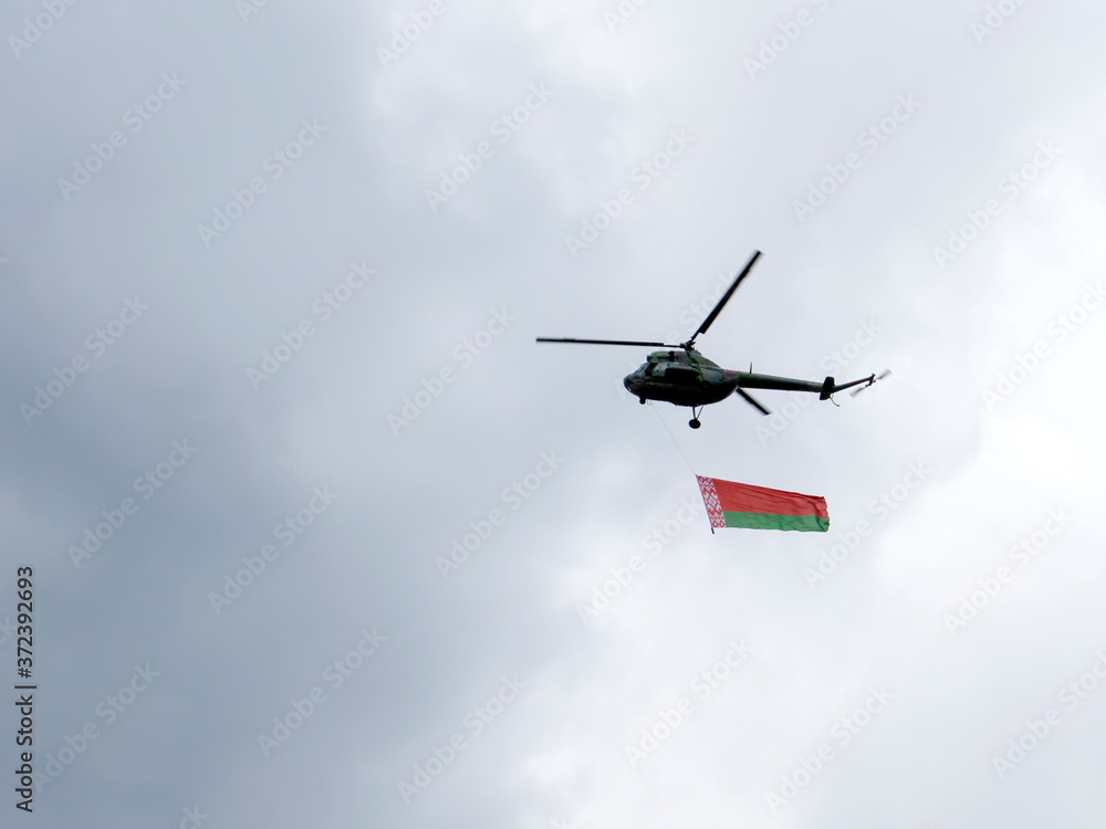 Fototapeta premium Helicopter flies in the sky with the Belarusian red-green flag. Political situation in Belarus