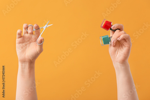 Female hands with manicure scissors and nail polishes on color background