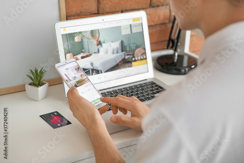 Man with mobile phone booking room in hotel online at home