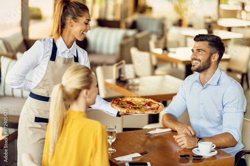 Happy waitress serving pizza to a couple in a restaurant.