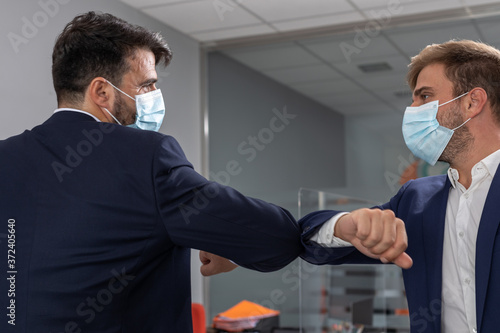 Two businessmen shaking hands with their elbows due to precautionary measures