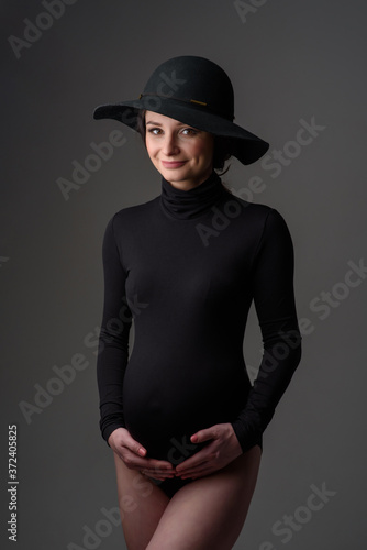 Young beautiful pregnant woman in black bodysuit and hat.