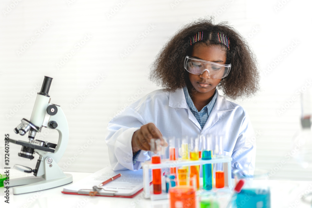 African american cute little girl student child learning research and doing a chemical experiment while making analyzing and mixing liquid in glass at science class on the table African american cute little girl student child learning research and doing a chemical experiment while making analyzing and mixing liquid in glass at science class on the table