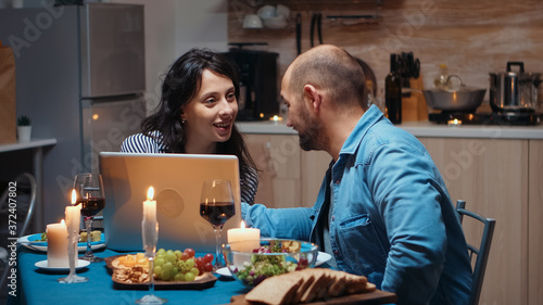 Excited caucasian lover couple dining together and using laptop. Adults sitting at the table, searching, browsing, surfing, using technology, enjoying the meal in the dining room