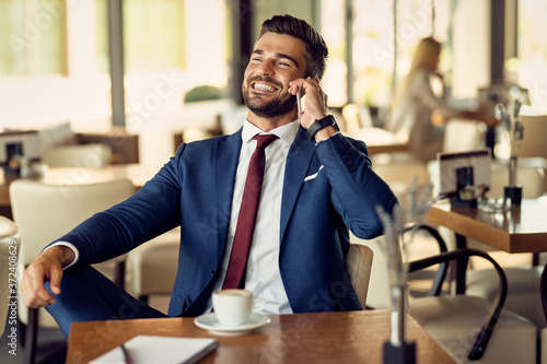 Happy mid adult businessman using cell phone on a coffee break in a cafe.