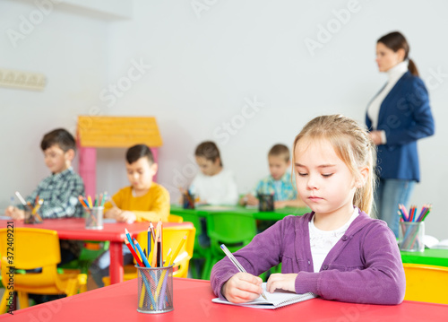 Portrait of assiduous little girl with pen and notebook at lesson in elementary school