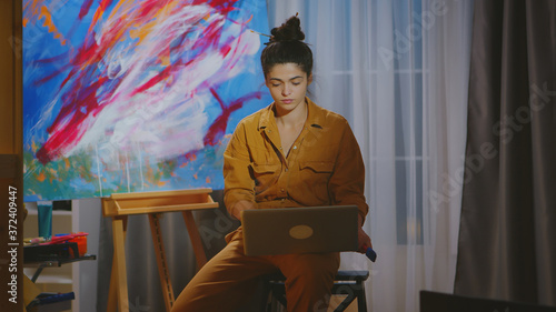 Painter searching inspiration on laptop in art studio.