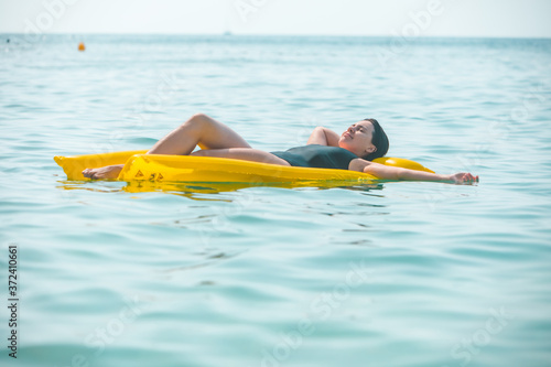 beautiful sexy woman laying on yellow inflatable mattress at sea water © phpetrunina14