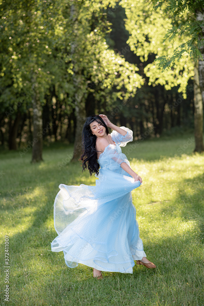 Pregnant woman posing in a blue dress on a background of green trees. Pregnant woman posing in a blue dress on a background of green trees.