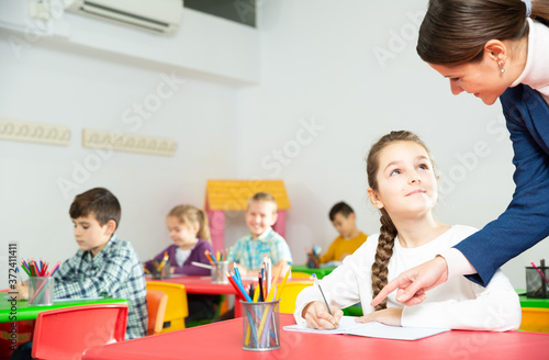 Friendly teacher woman helping girl during lesson in schoolroom. High quality photo