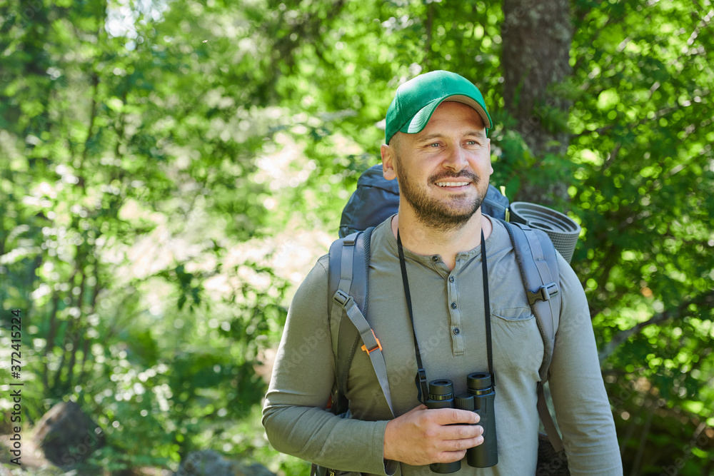 Mature man with backpack behind his back and binoculars happy with his trip in the forest