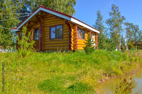 wooden house made of beams and boards in a Russian village, field, pond and blue sky