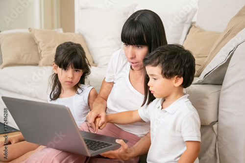 Mom teaching kids to use laptop, holding hand of little son and pressing keyboard button with boy finger. Medium shot. Parenthood and modern technology concept © Mangostar