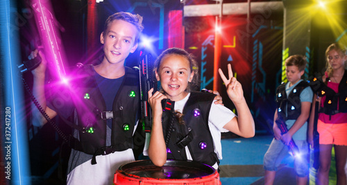 Portrait of happy teenager girl and boy with laser guns on dark lasertag arena..