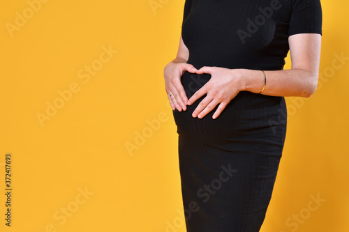 Pregnant woman holding her belly on yellow background