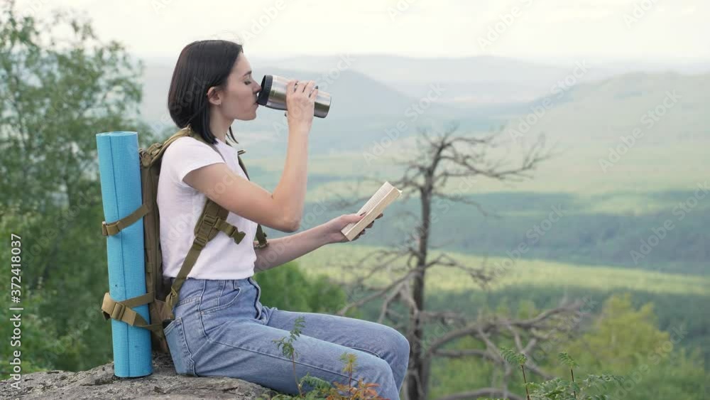The girl is sitting on the edge of the mountain, reading a book and resting. The girl is sitting on the edge of the mountain, reading a book and resting.
