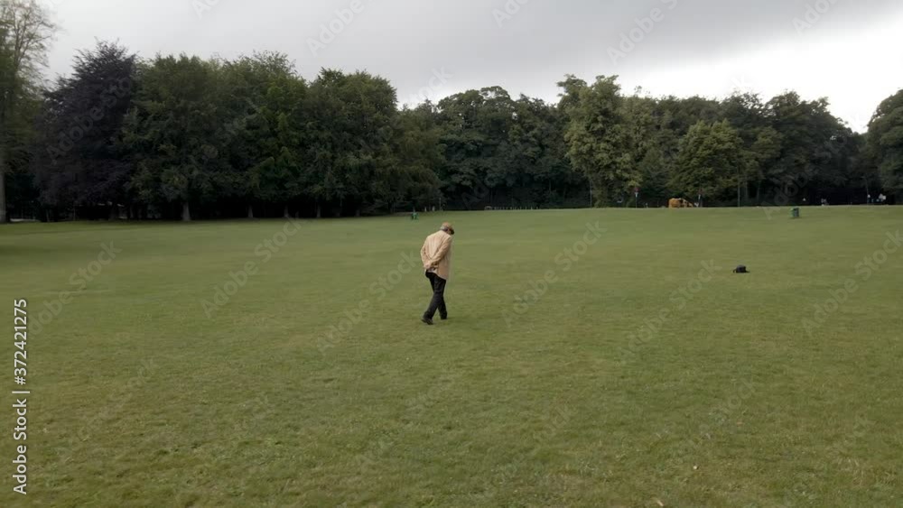 Elderly man walking alone through park field, aerial arc shot Elderly man walking alone through park field, aerial arc shot