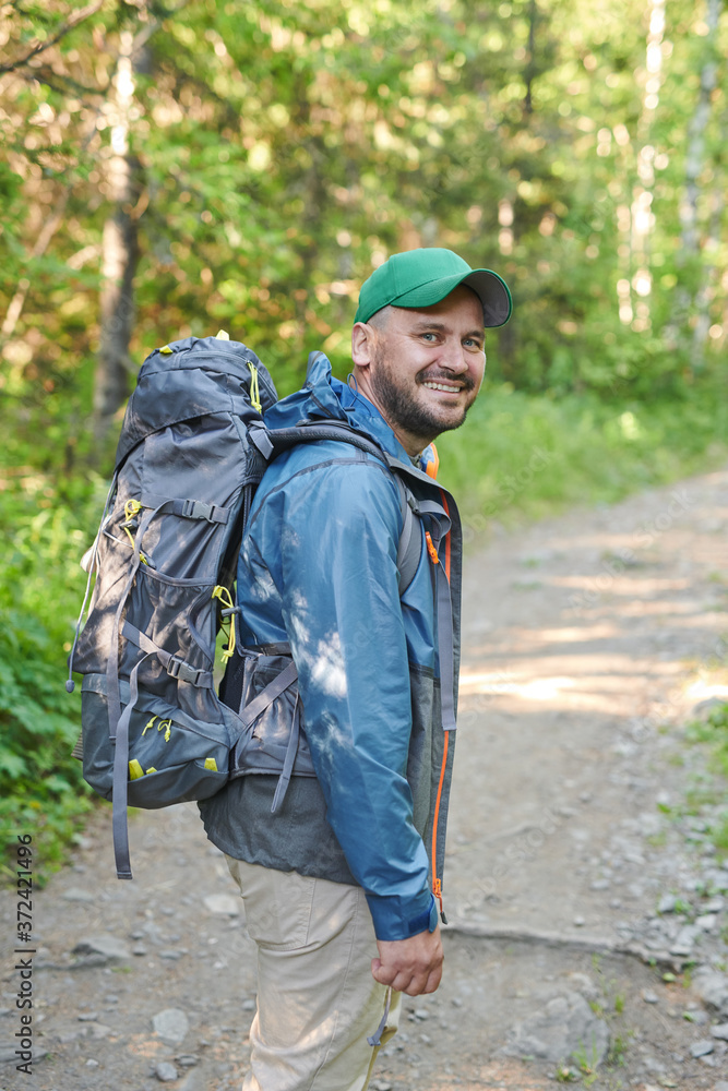 Portrait of mature man with backpack smiling at camera while hiking in the forest Portrait of mature man with backpack smiling at camera while hiking in the forest