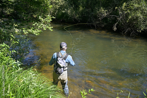 fly fisherman in summer fishing in a mountain river with waders and a cap