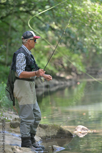 fly fisherman in summer fishing in a mountain river with waders and a cap