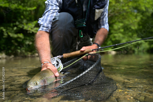 fly fisherman in summer catching a rainbow trout fishing in a mountain river