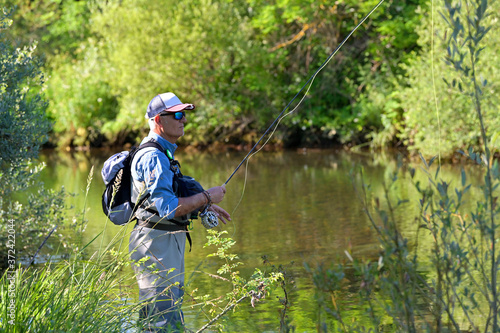 fly fisherman in summer fishing in a mountain river with waders and a cap