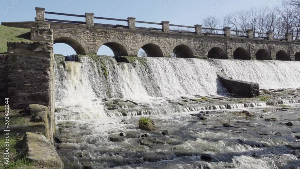 A low bridge across a small waterfall with a river in a rural area on a sunny day - front view